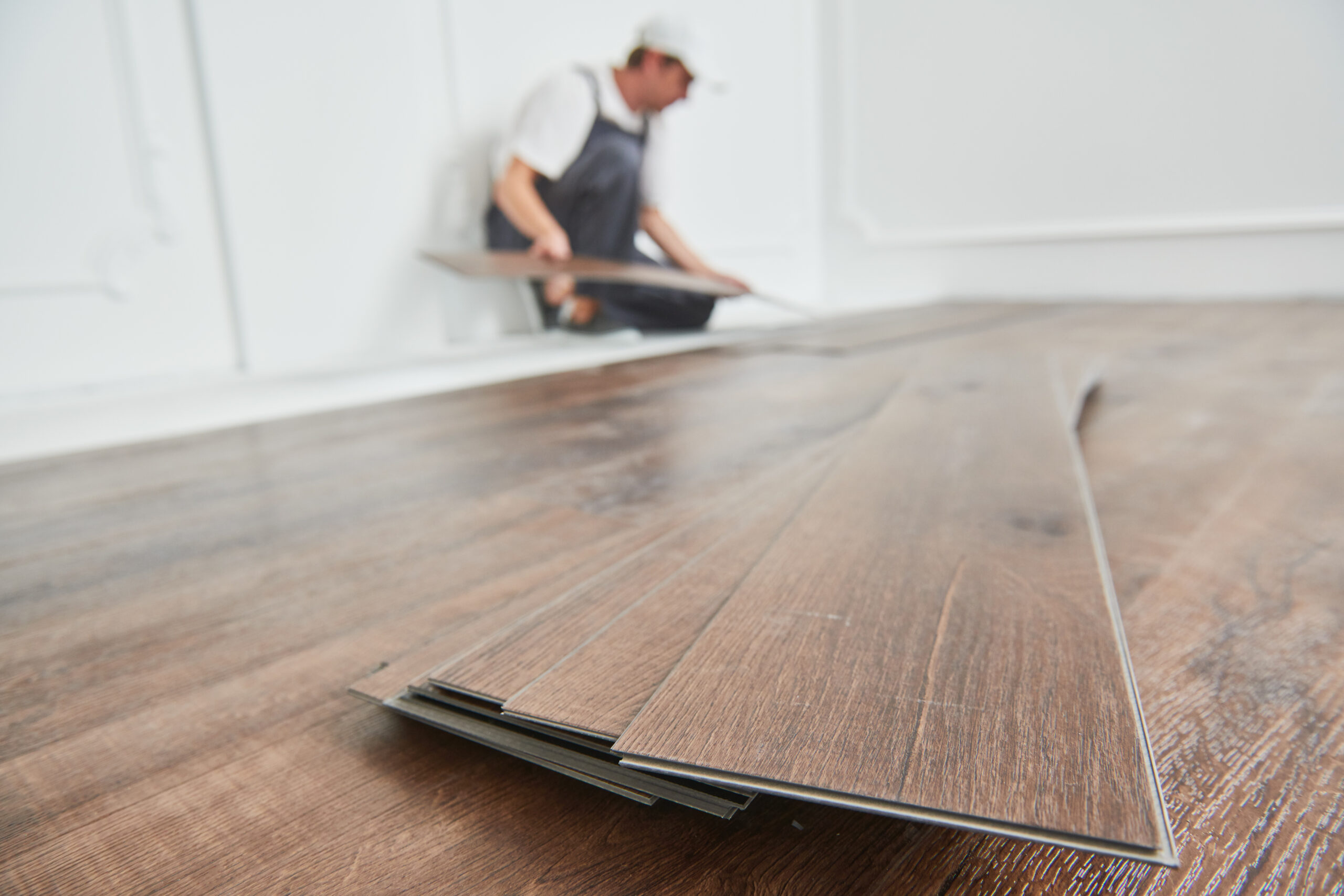 Worker laying vinyl plank flooring, with loose planks in the foreground