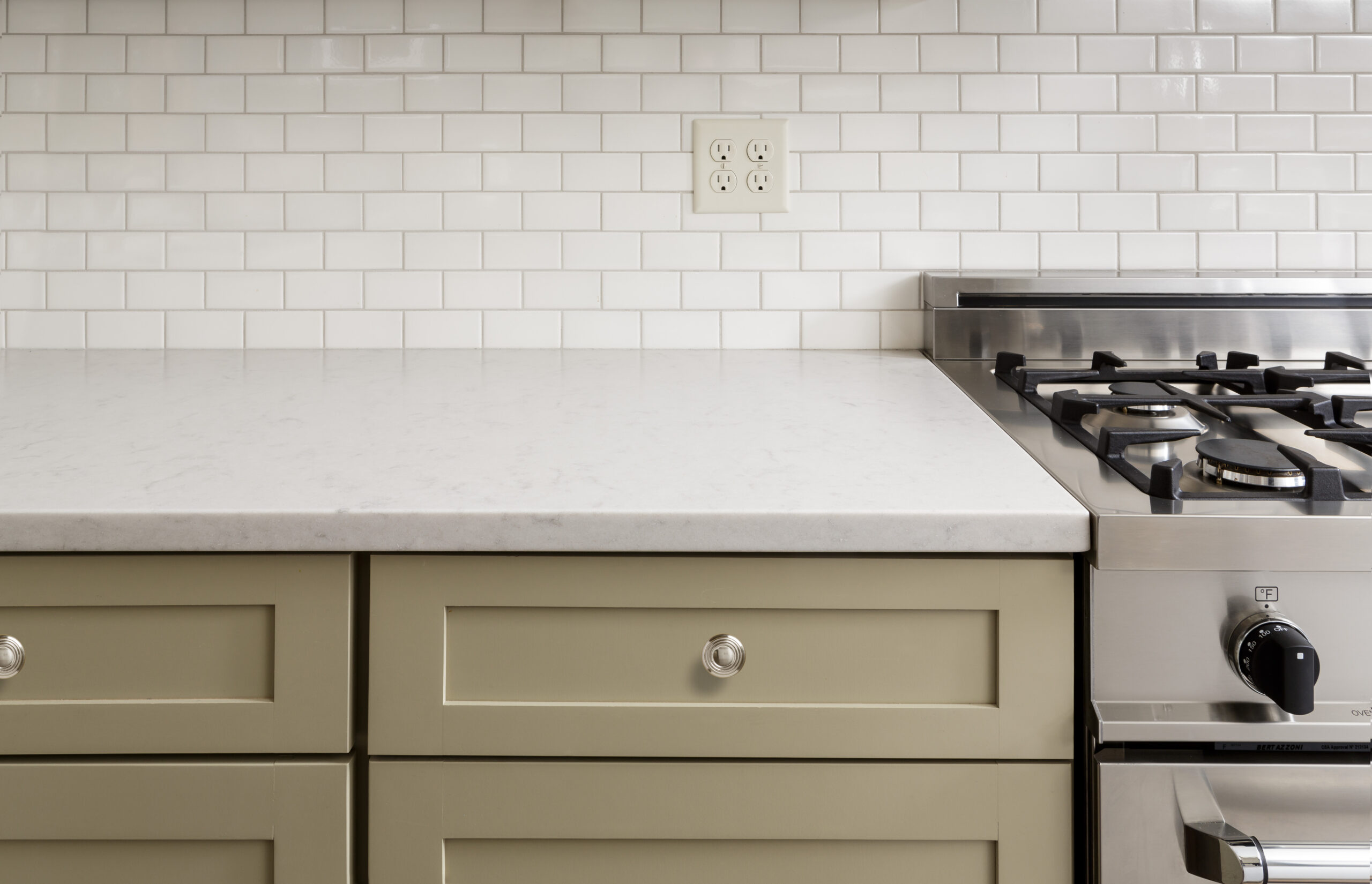Olive green kitchen cabinets with white subway tile, marble counter and a gas range