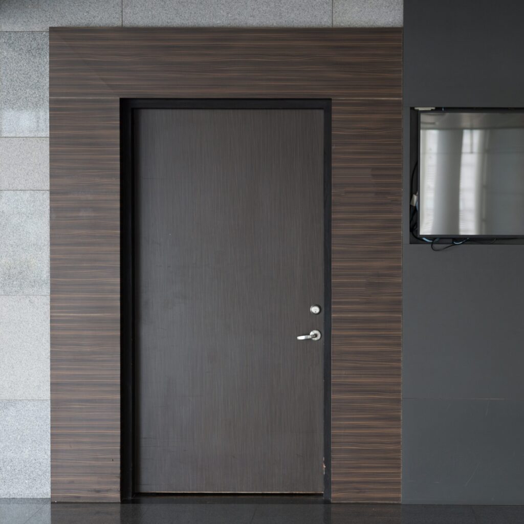 Grey flush door set in a dark wood panelled wall