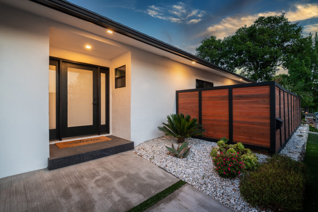 White stucco home entry at dusk with a black full-lite door and a wood fence