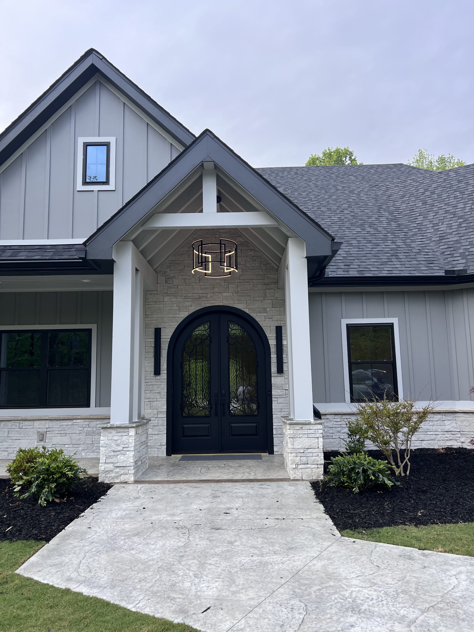 Light grey board-and-batten home with arched black double entry doors and house number 52