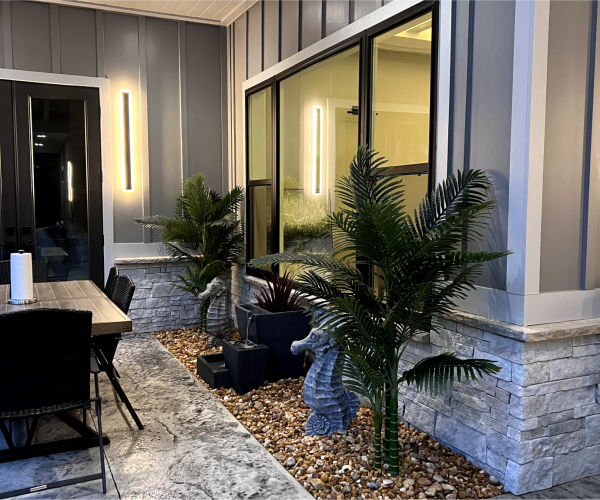 Covered patio with black-framed windows, linear wall lights, palms and a gravel bed