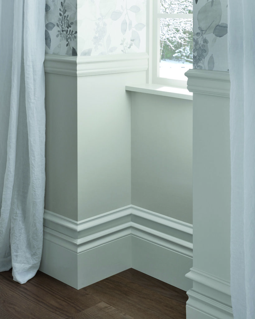 Corner of a room showing white painted baseboard, chair rail and window trim