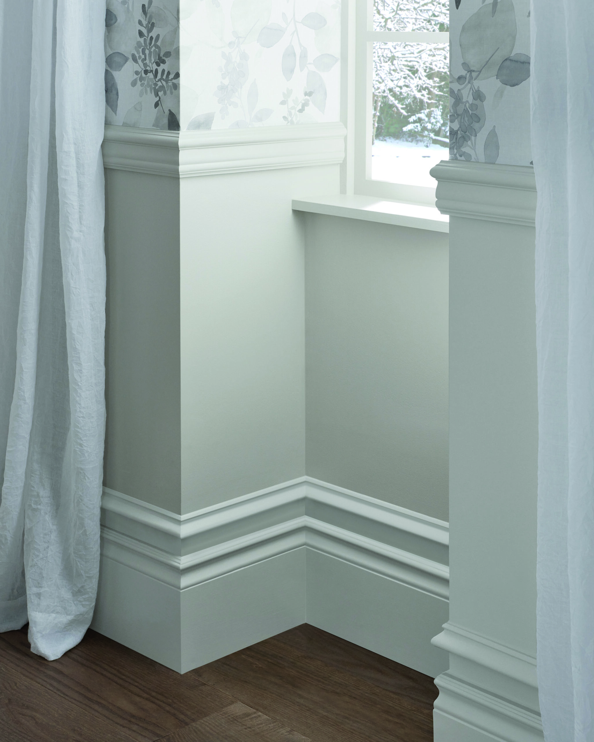Corner of a room showing white painted baseboard, chair rail and window trim