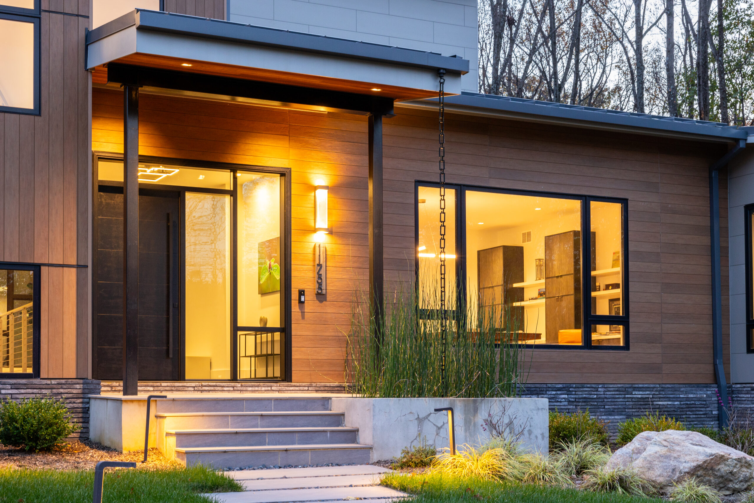 Modern home at dusk with wood siding, a full-lite glass entry door and large windows