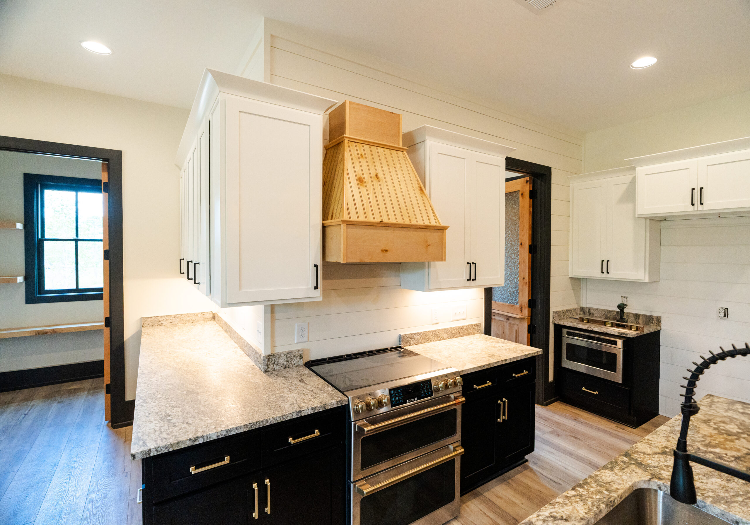 Kitchen with white upper cabinets, black lower cabinets and a wood range hood