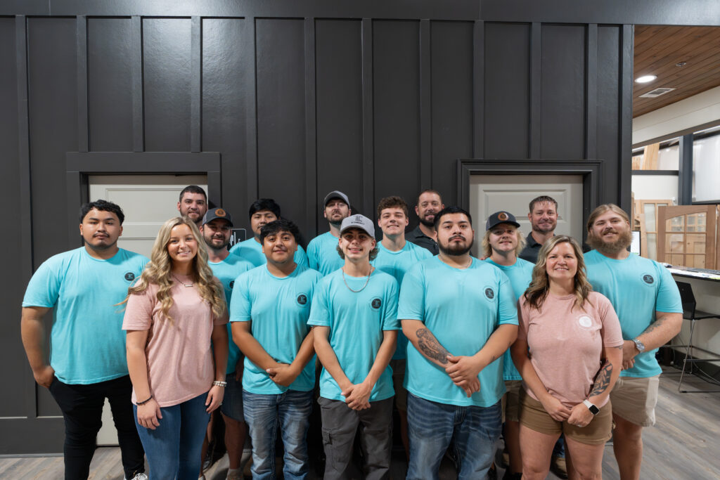 Group of TLC Elite team members in teal shirts in front of a dark board-and-batten wall