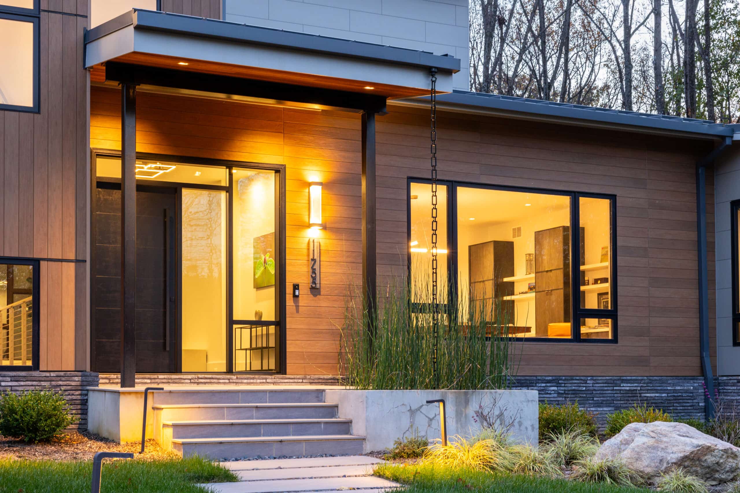 Modern home at dusk with wood siding, a full-lite glass entry door and large windows