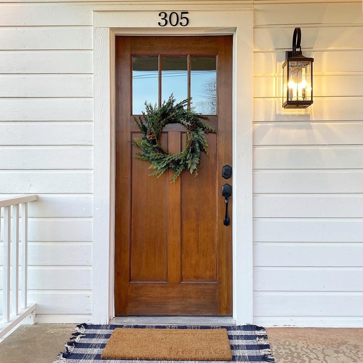 White siding entry with a stained wood craftsman door, wreath and house number 305