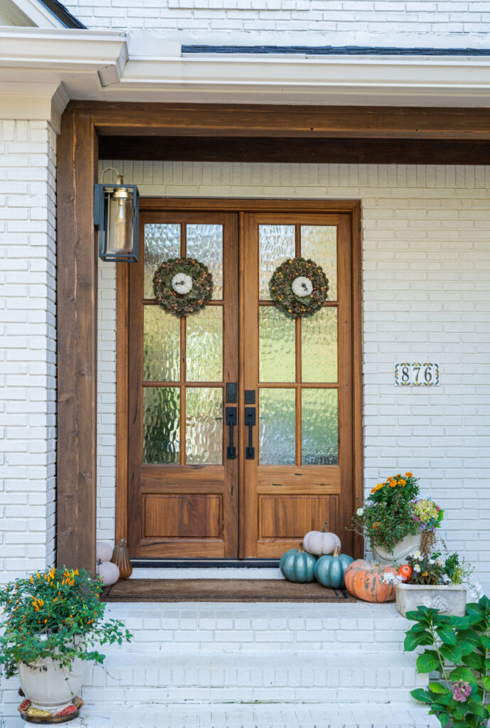 White brick entry with wood double doors with textured glass, wreaths and pumpkins