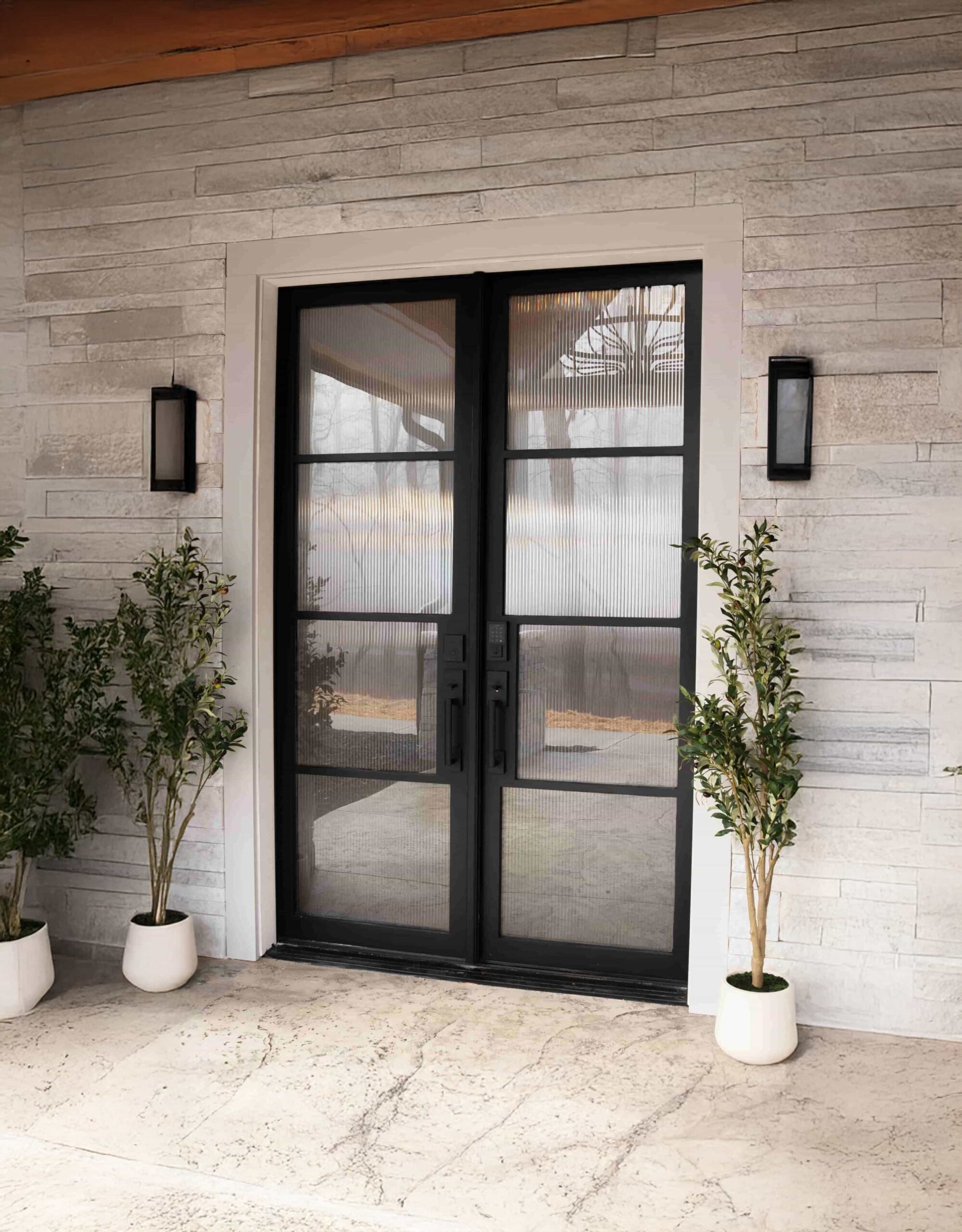 Black full-lite double entry doors flanked by potted olive trees