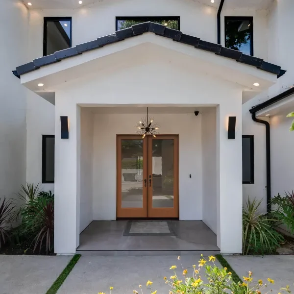 White stucco home entry with light wood double doors under a portico