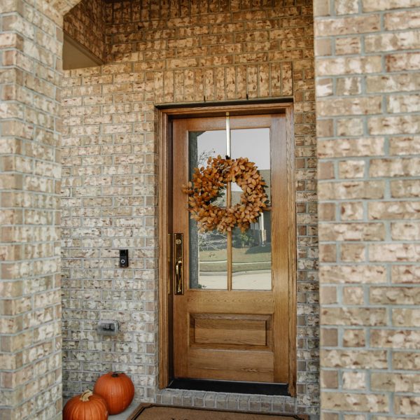 Brick entry with a wood half-lite front door, an autumn wreath and pumpkins