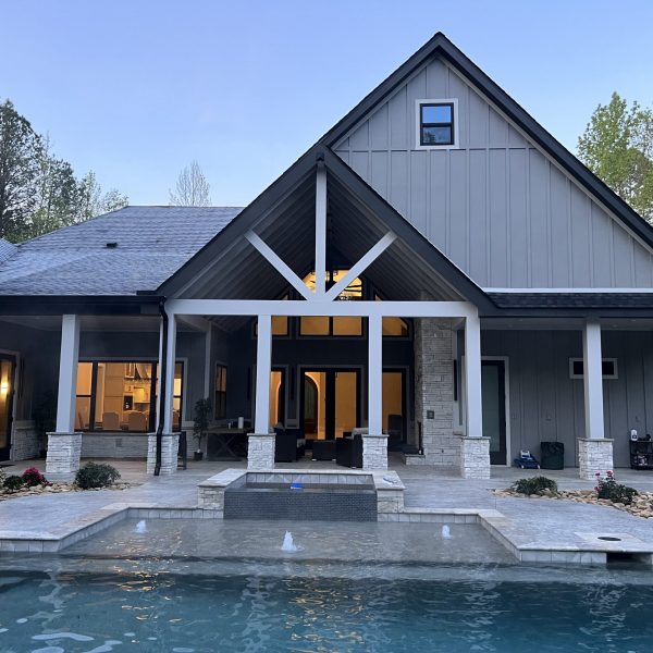 Rear of a grey home at dusk with a gabled covered patio and a swimming pool